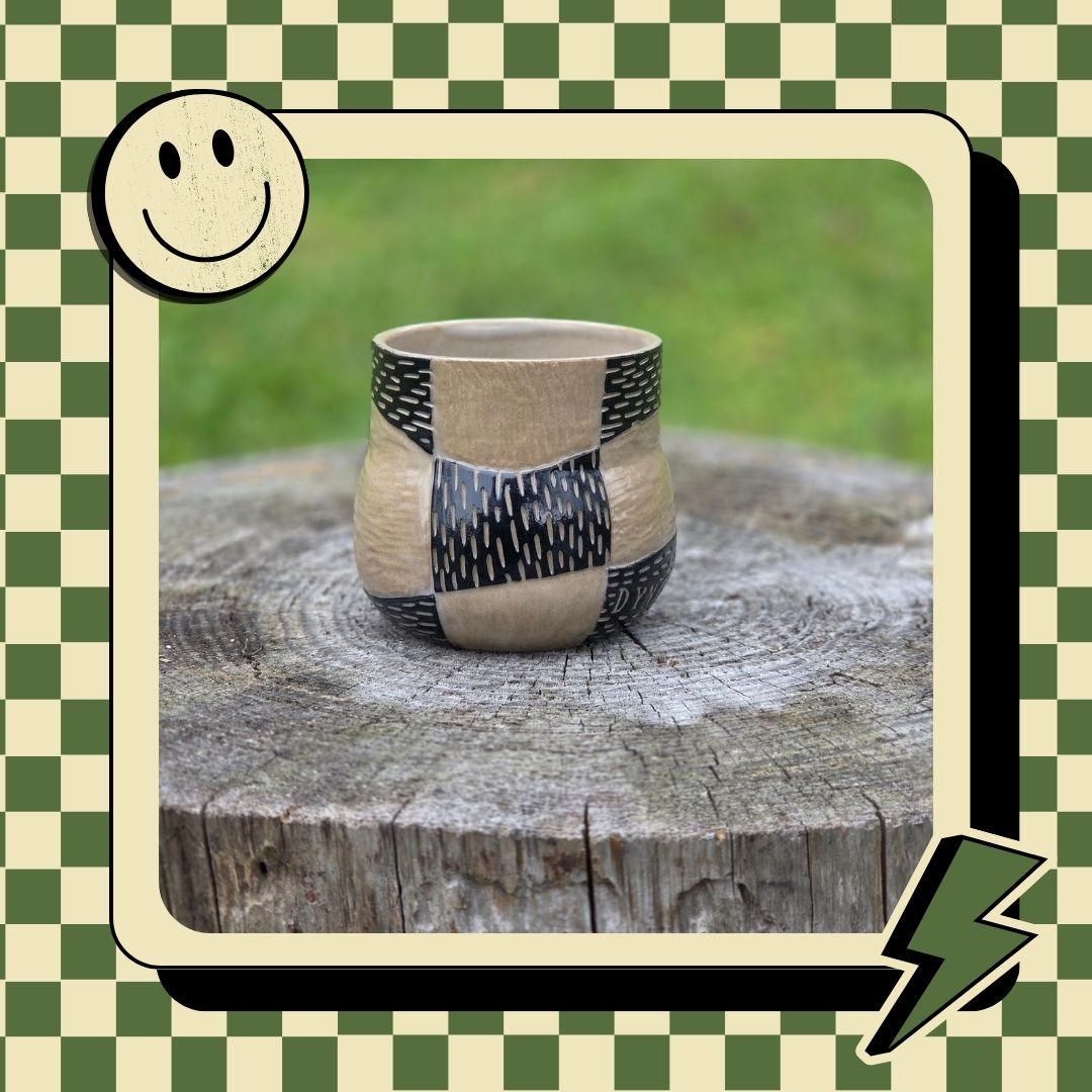 Ceramic cup with black pattern on a wooden stump against a green checkered border