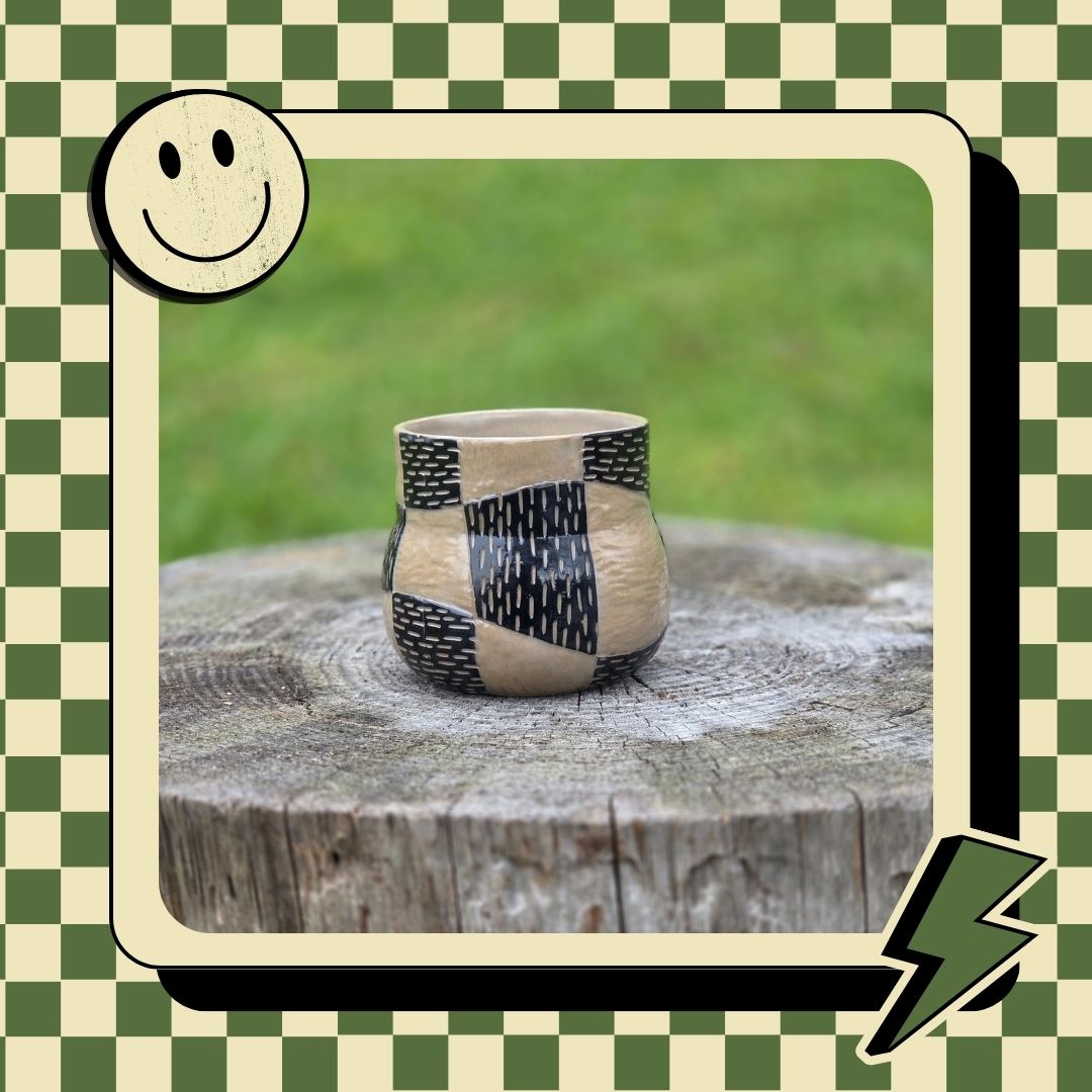 Ceramic cup with black pattern on a wooden stump against a green grass background, framed with decorative elements.
