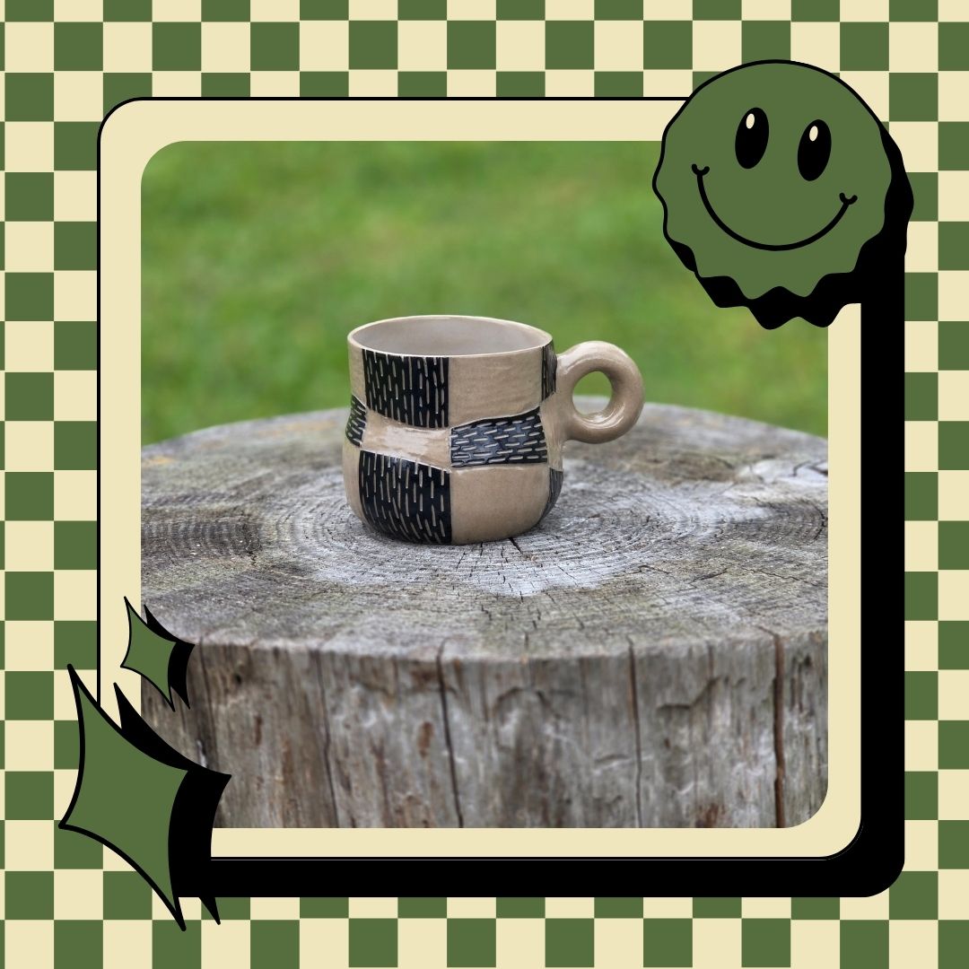 Ceramic mug with black pattern on a wooden stump against a green checkered background