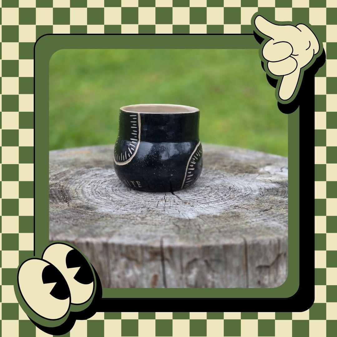 Black ceramic cup with decorative patterns on a wooden stump, framed by a green and white checkered border.