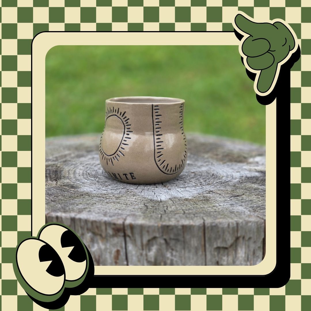 Ceramic cup with sun design on a wooden stump, framed by decorative elements on a green and white checkered background.